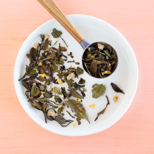 Peachy Keen White Tea shown as loose leaf tea in a scoop on a white plate with more loose leaf tea.