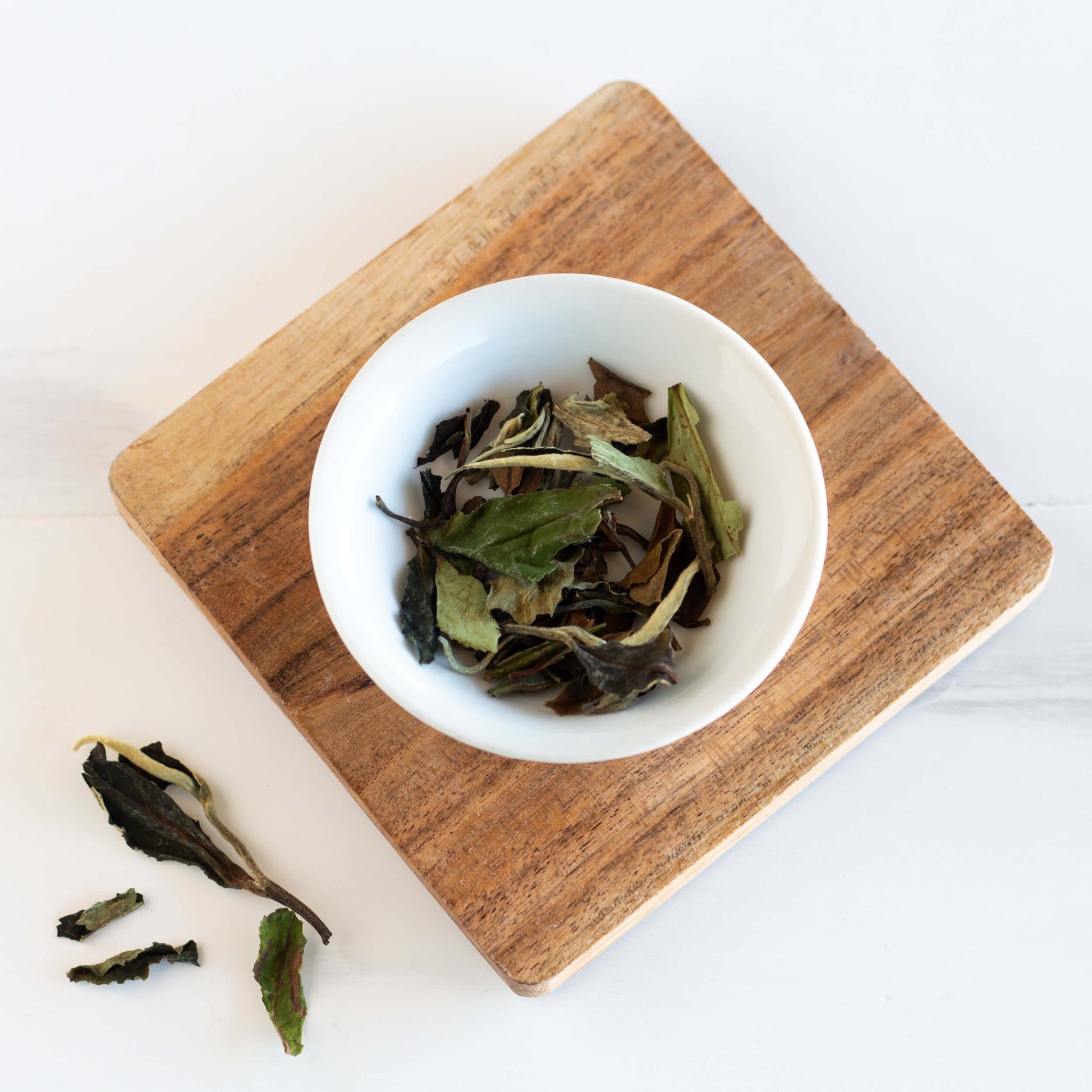 White Peony White Tea shown as loose leaf tea in a small white dish on top of a wooden coaster.