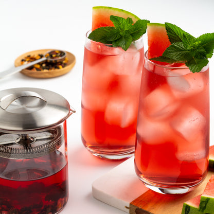Sandia Sangria Oolong Tea shown as iced tea in two glasses with slices of watermelon and sprigs of mint. A glass teapot of brewed tea is in the foreground