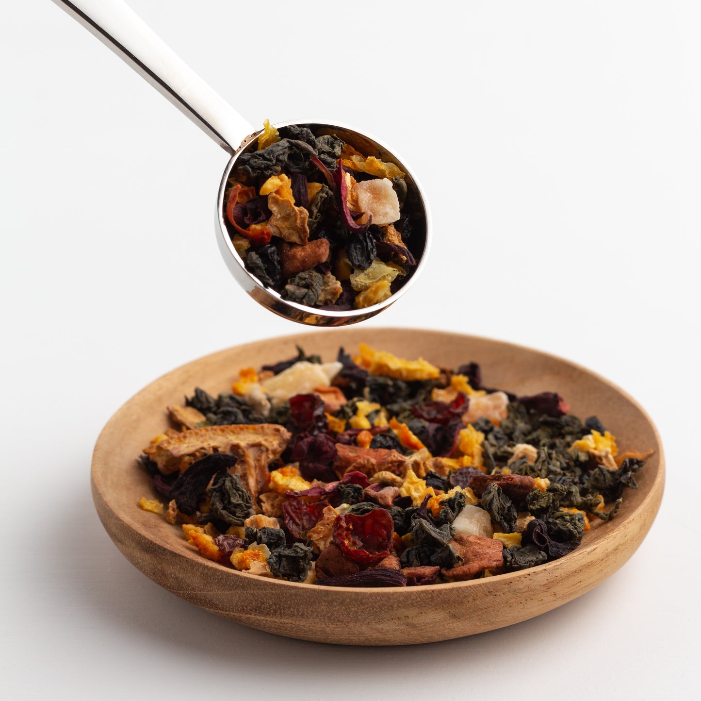 Sandia Sangria Oolong Tea displayed as loose tea in a small wooden dish with a stainless steel scoop of loose tea in the air above the dish