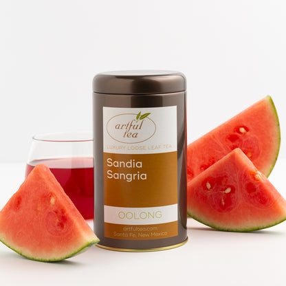 Sandia Sangria Oolong Tea shown packaged in a brown tin, surrounded by slices of watermelon, and a glass of brewed tea in the background