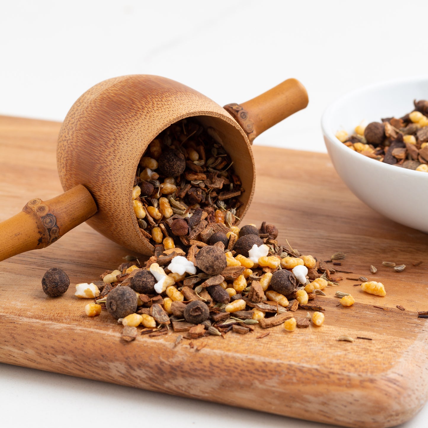 Horchata Rooibos Herbal Tea shown as loose tea displayed on a wooden board, and also spilling from a bamboo strainer