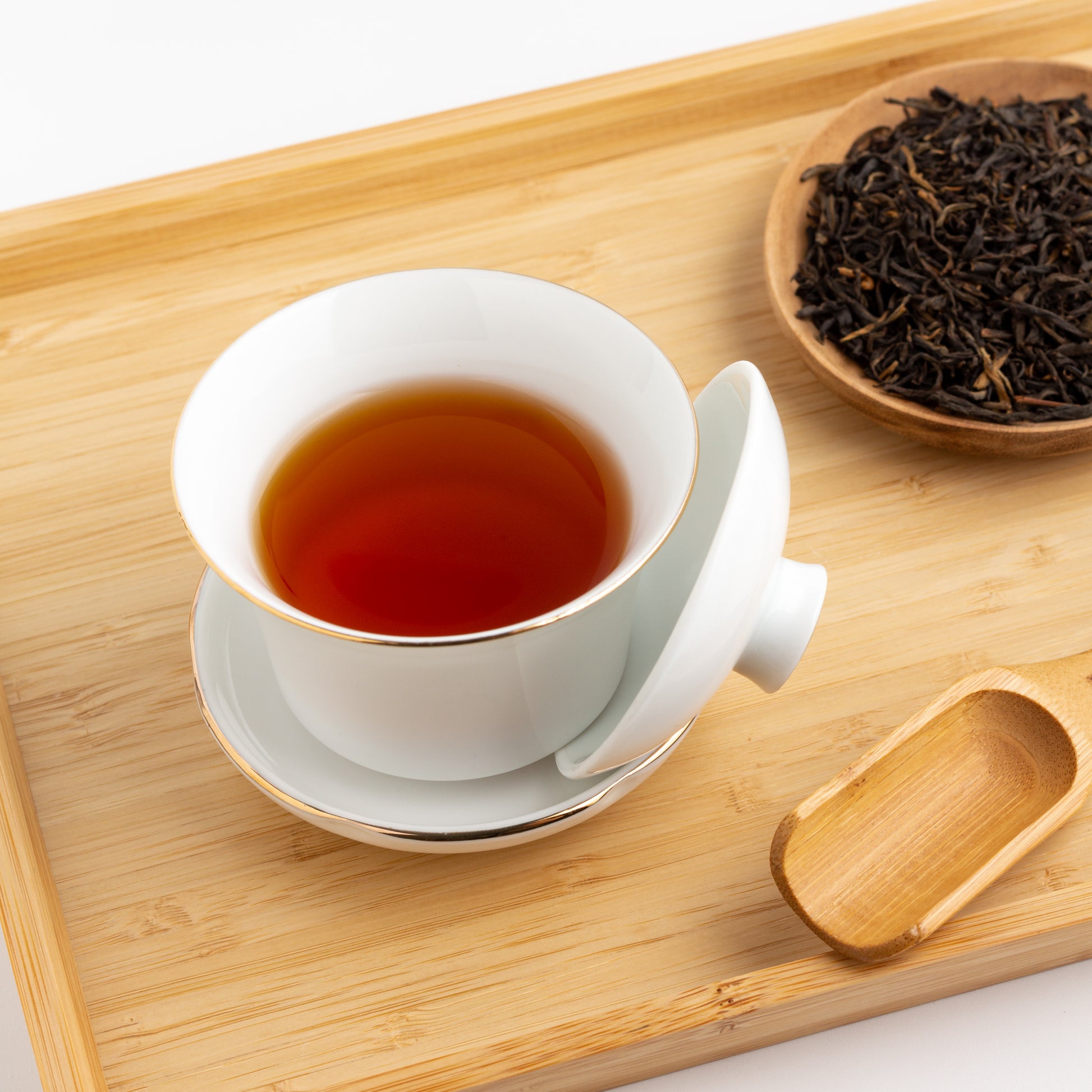 Golden Yunnan Organic Black Tea shown brewed in a white gaiwan cup on a wooden tray.
