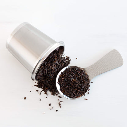 Organic Ceylon Black Tea shown as loose leaf tea spilling out of a stainless steel infuser, with a scoop full of tea leaves nearby