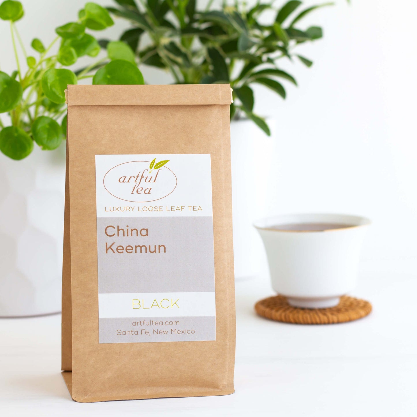 China Keemun Black Tea shown packaged in a kraft bag, with white cup and green plants in the background