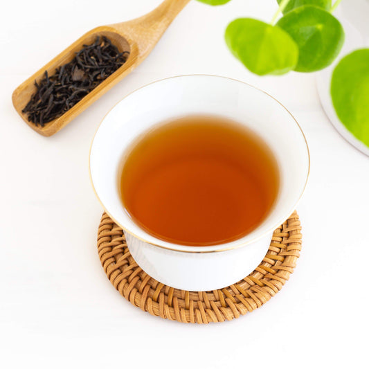 China Keemum Black Tea shown from above as brewed tea in a white gaiwan cup, with a wooden scoop of loose tea leaves in upper left corner