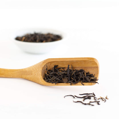China Keemun Black Tea shown as loose tea leaves in a wooden scoop, with a white dish of tea leaves in the background
