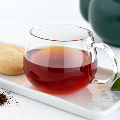 Irish Breakfast Organic Black Tea shown as brewed tea in a glass mug, displayed on a white ceramic tray with a shortbread cookie