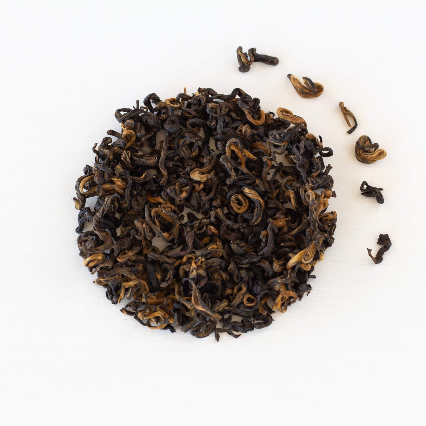 Nepalese Gold Black Tea shown from above as loose tea leaves in a tight circle with a few leaves to the right of the circle