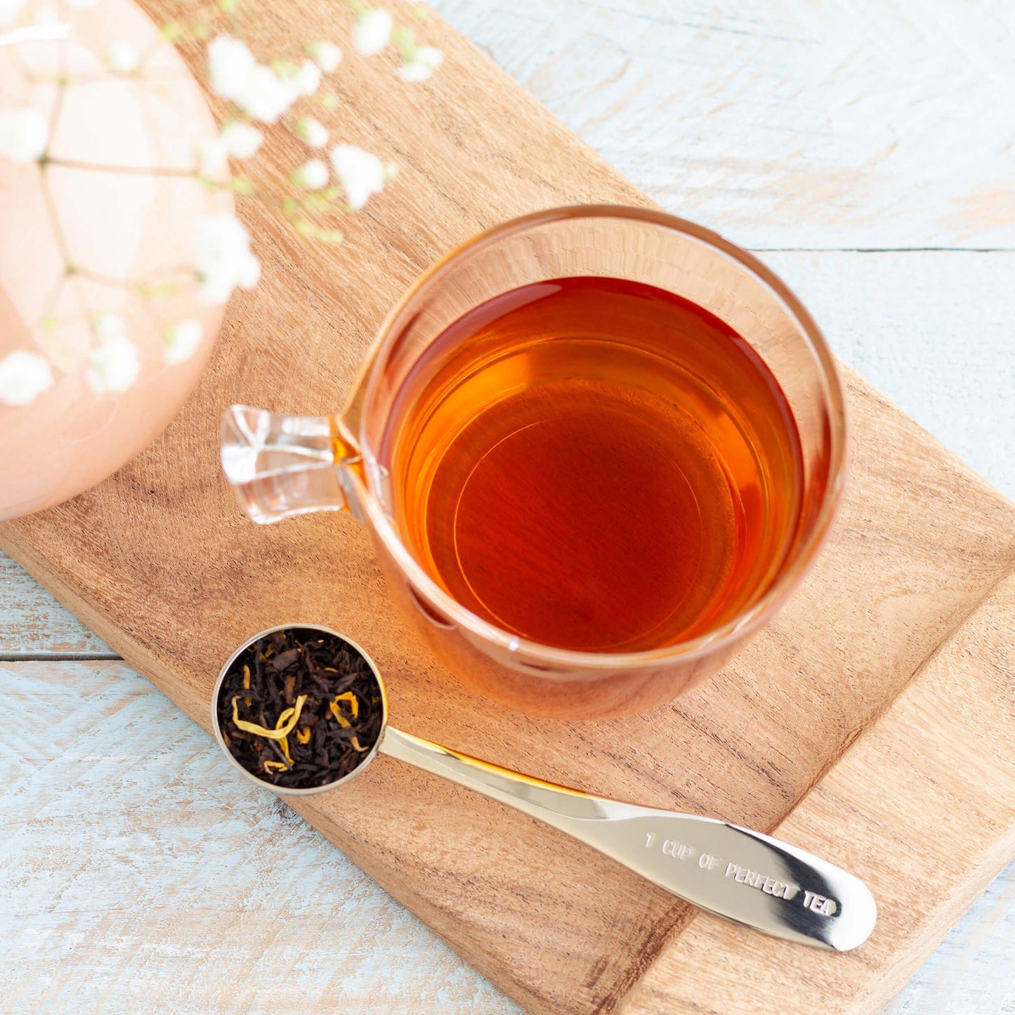 Apricot Brandy Organic Black Tea shown from above as brewed tea in a glass mug, displayed on a wooden board with a silver scoop of loose tea leaves in front