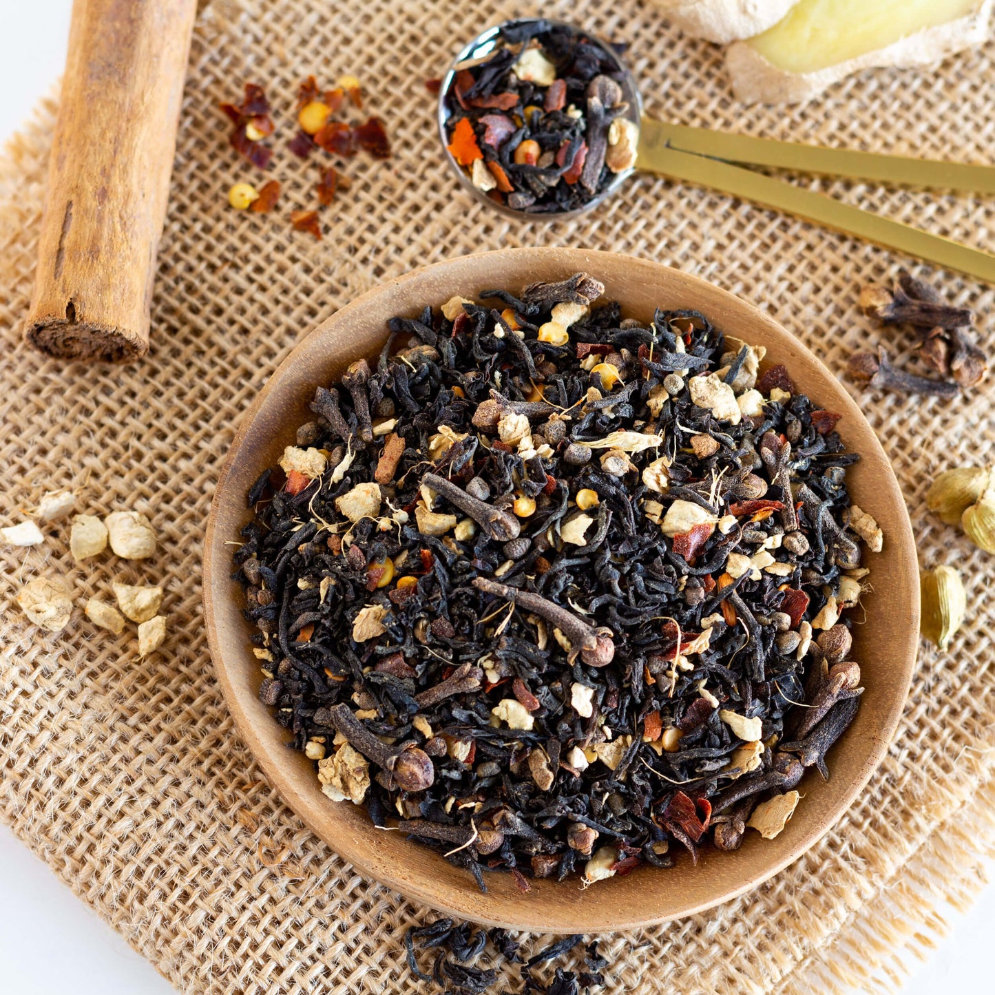 Chimay Chai Black Tea shown from above as loose tea leaves and ingredients in a small wooden bowl on a background of tan burlap.