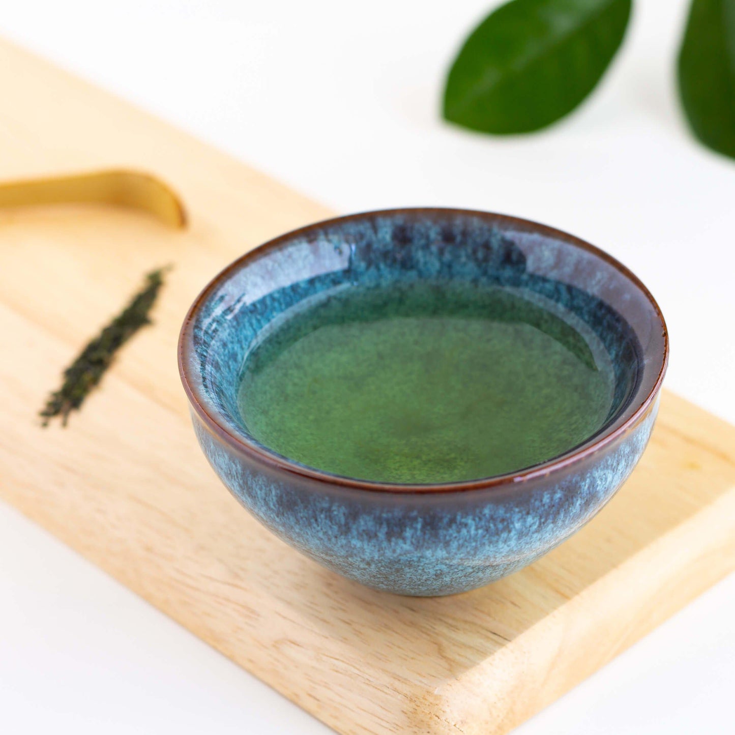 Gyokuro Green Tea shown as brewed tea in a small teal blue teacup displayed on a bamboo plank