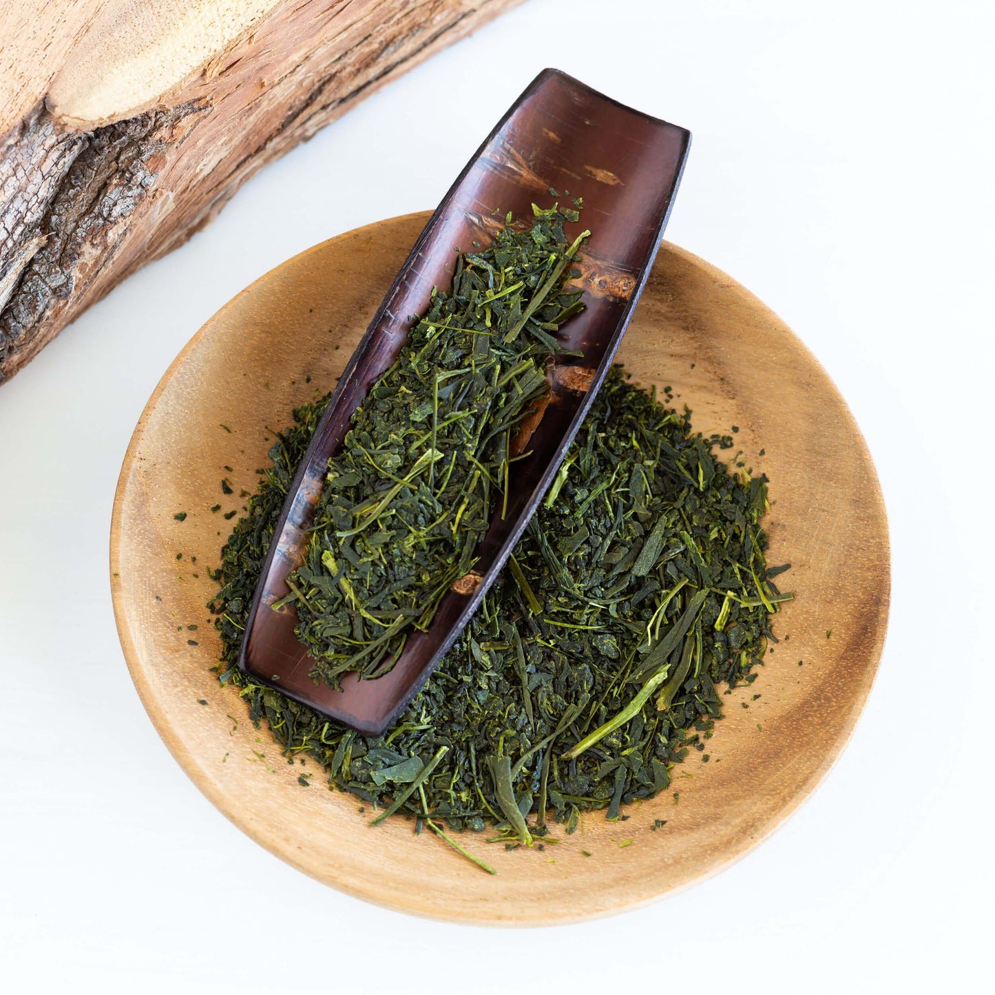 Shincha Green Tea shown from above as loose tea leaves in a Japanese cherry wood scoop and in a small wooden dish.