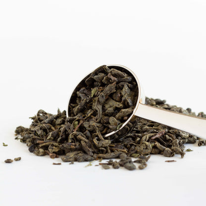 Moroccan Mint Green Tea shown in close up as loose tea leaves spilling out of a silver tea scoop