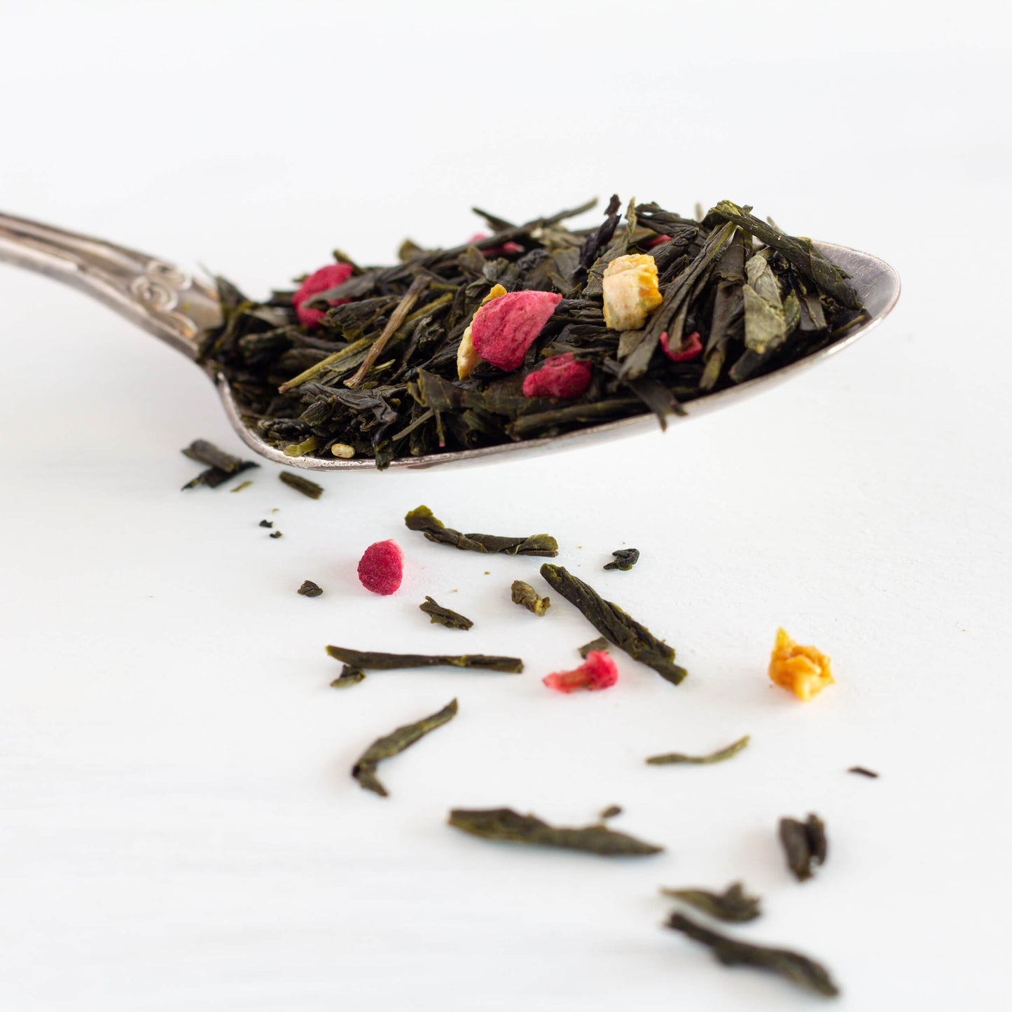 Raspberry Orange Rhapsody Green Tea shown as loose tea leaves in a silver spoon