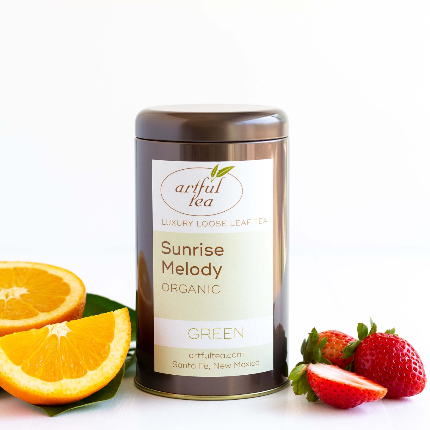 Sunrise Melody Organic Green Tea shown packaged in a brown tin, with strawberries and wedges of orange nearby