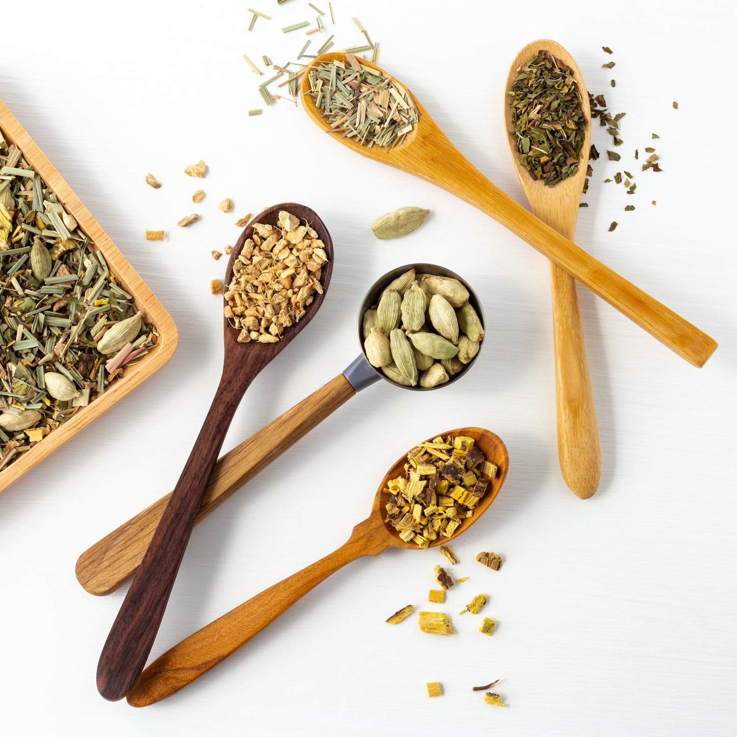 Sing Your Song organic herbal tea ingredients shown in wood spoons (peppermint, ginger, cardamom pods, licorice root, and lemongrass)