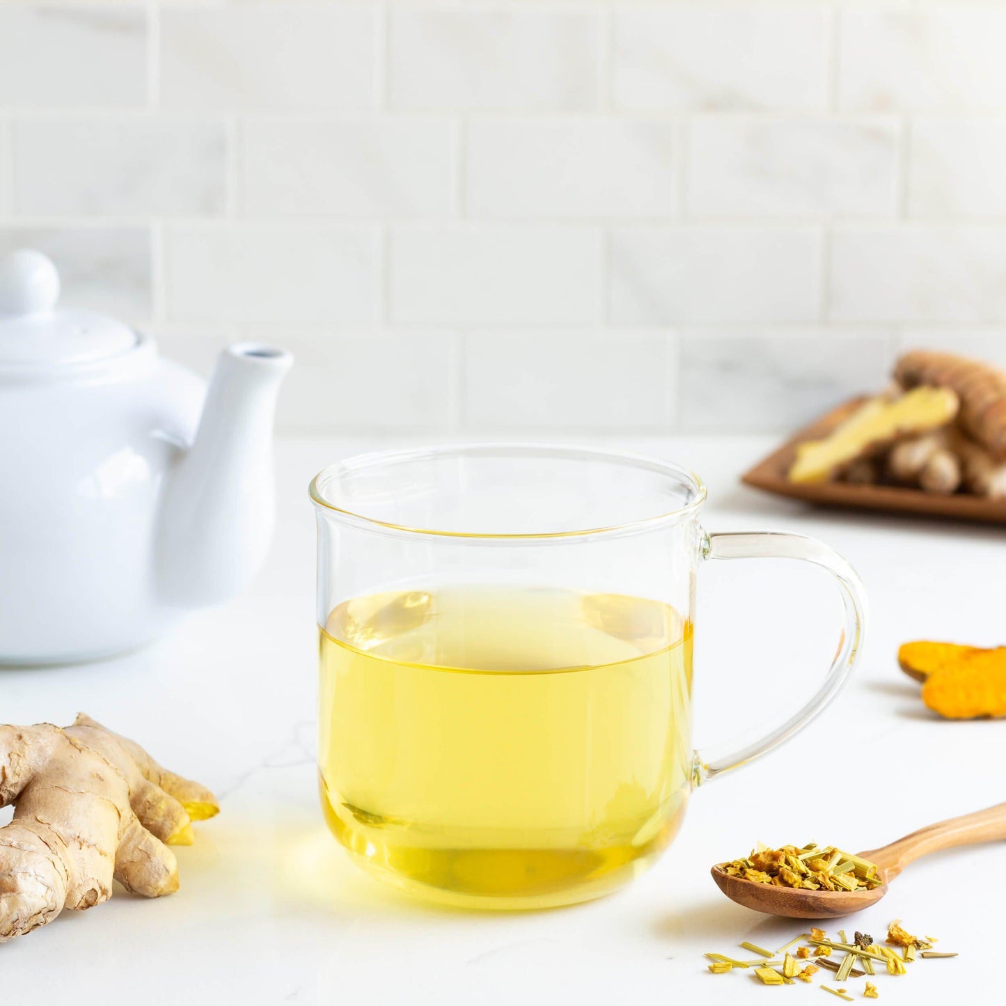 Atomic Gold Organic Herbal Tea shown as brewed tea in a glass mug with ginger root and sliced turmeric root nearby