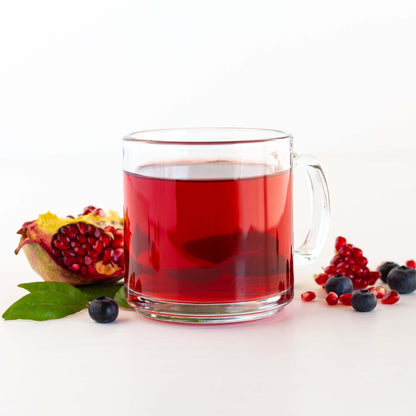 Blueberry Pomegranate Herbal Tea shown brewed in a glass mug, with blueberries and an open pomegranate nearby