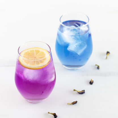 Butterfly Pea Flower Herbal Tea shown as iced tea in two glasses. In one the tea is blue, in the other the tea has a slice of lemon in it and has turned purple