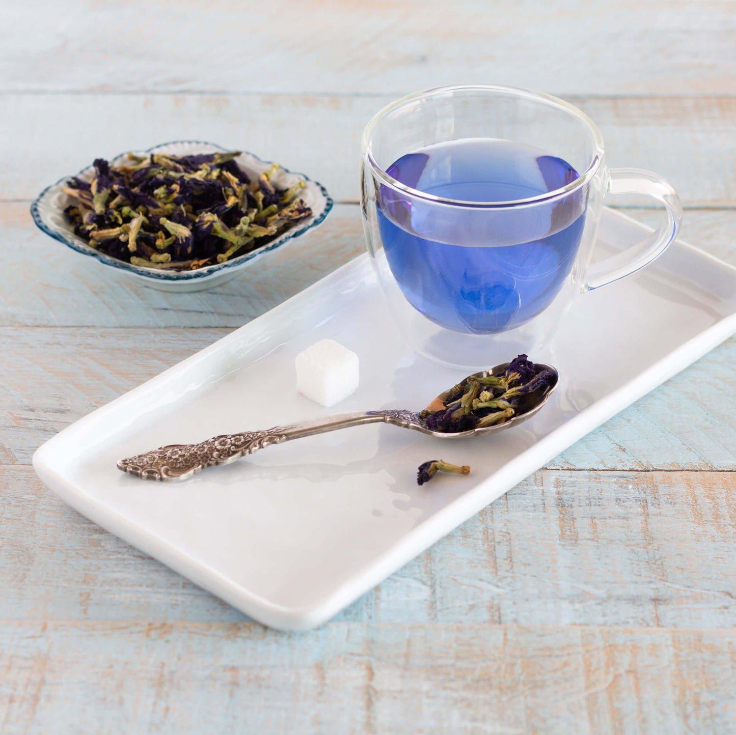 Bowl of loose-leaf Butterfly Pea Flower Herbal Tea with glass mug on tray