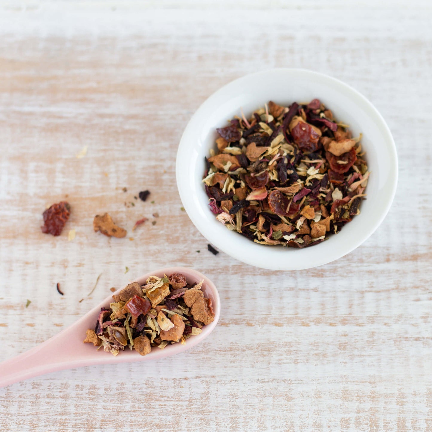 Raspberry Lemonade Organic Herbal Tea shown from above as loose tea leaves in a small white bowl with a white ceramic spoon of tea leaves