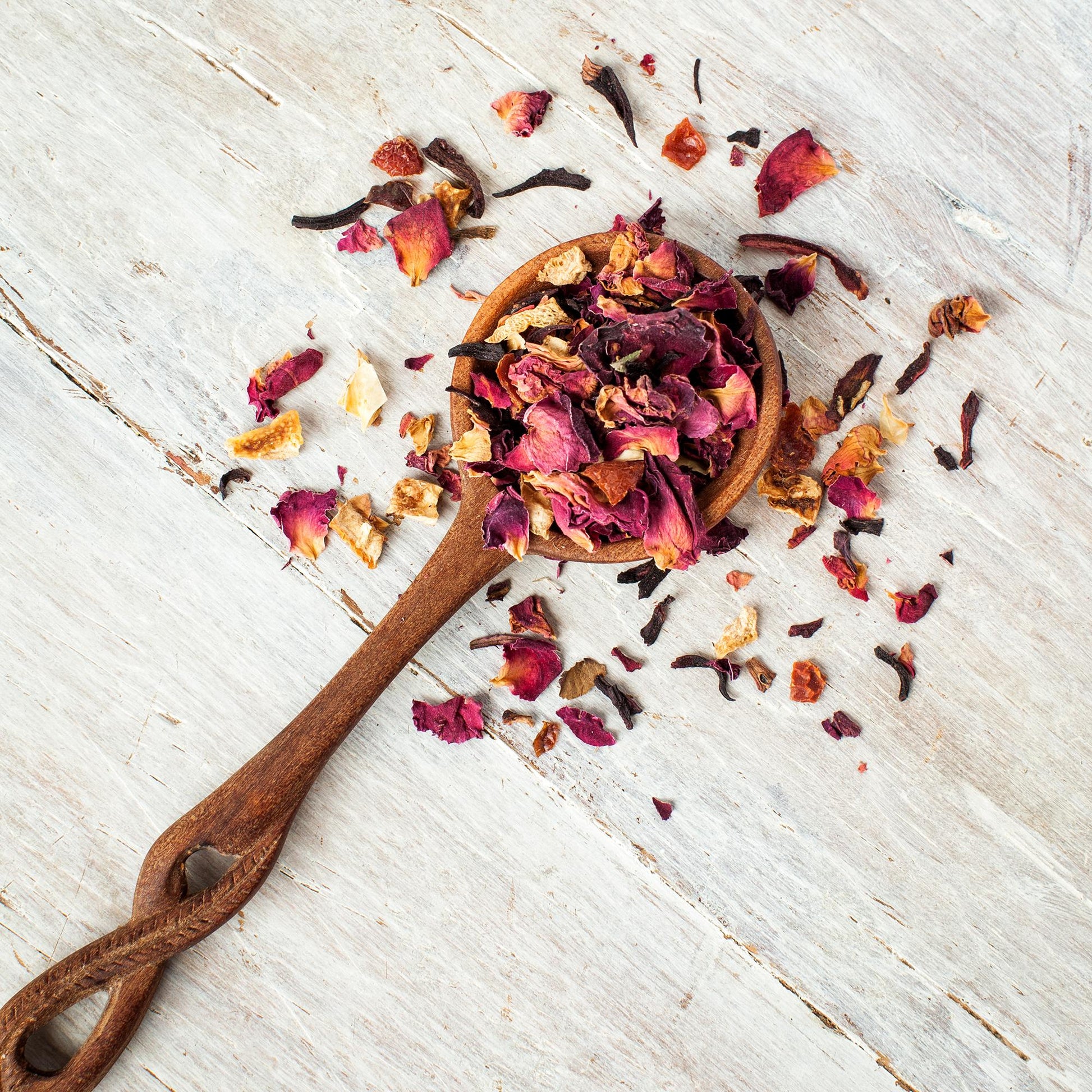 Rose Petal Raspberry Herbal Tea shown from above as loose tea leaves in a wooden spoon with an elaborate carved handle