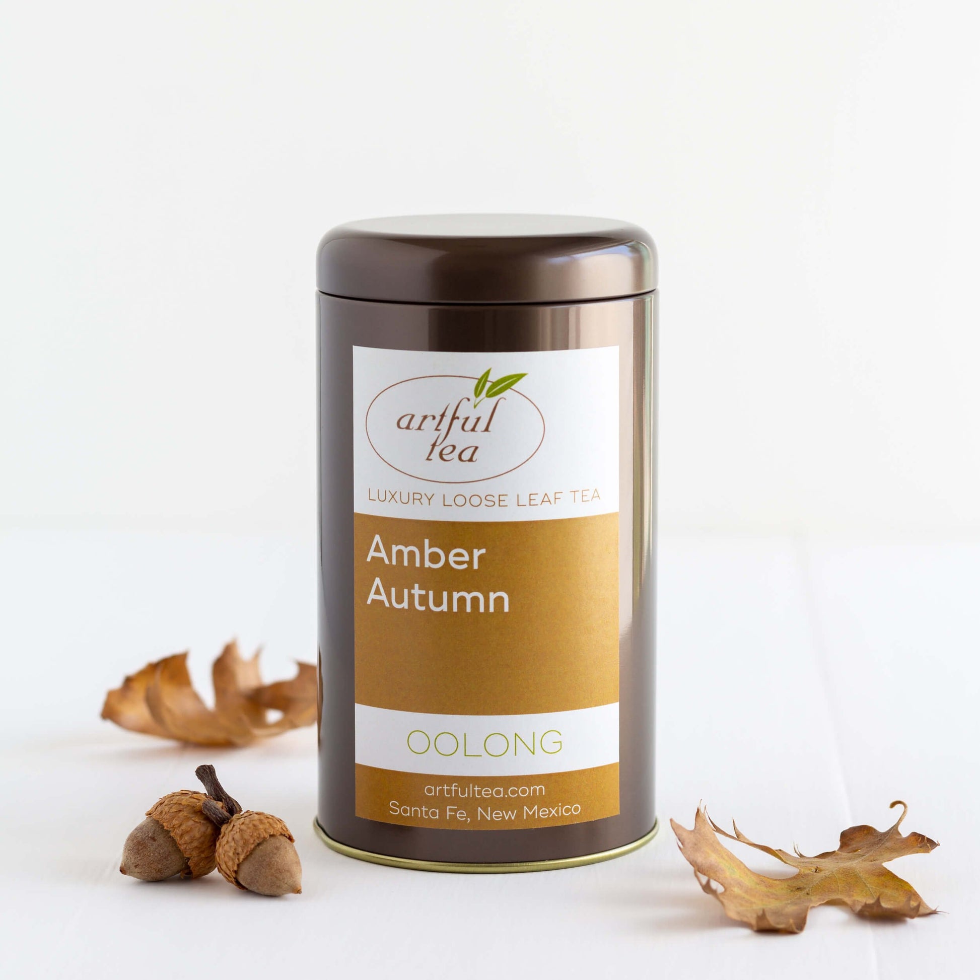 Amber Autumn Oolong shown packaged in a brown tin, with two acorns and two brown tree leaves nearby.