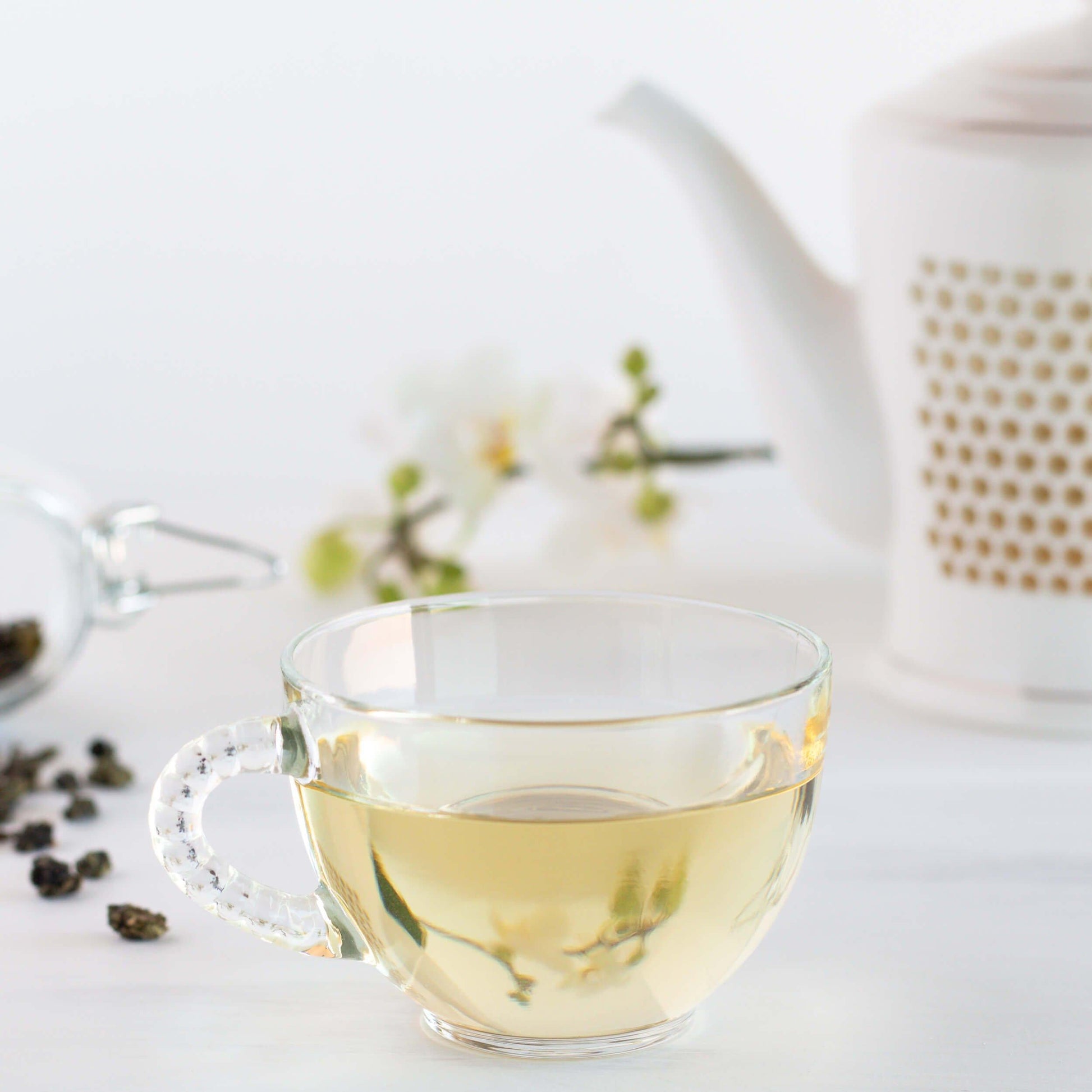 Fine Ti Kuan Yin Organic Oolong Tea shown as brewed tea in a glass teacup with a white and gold teapot in the background