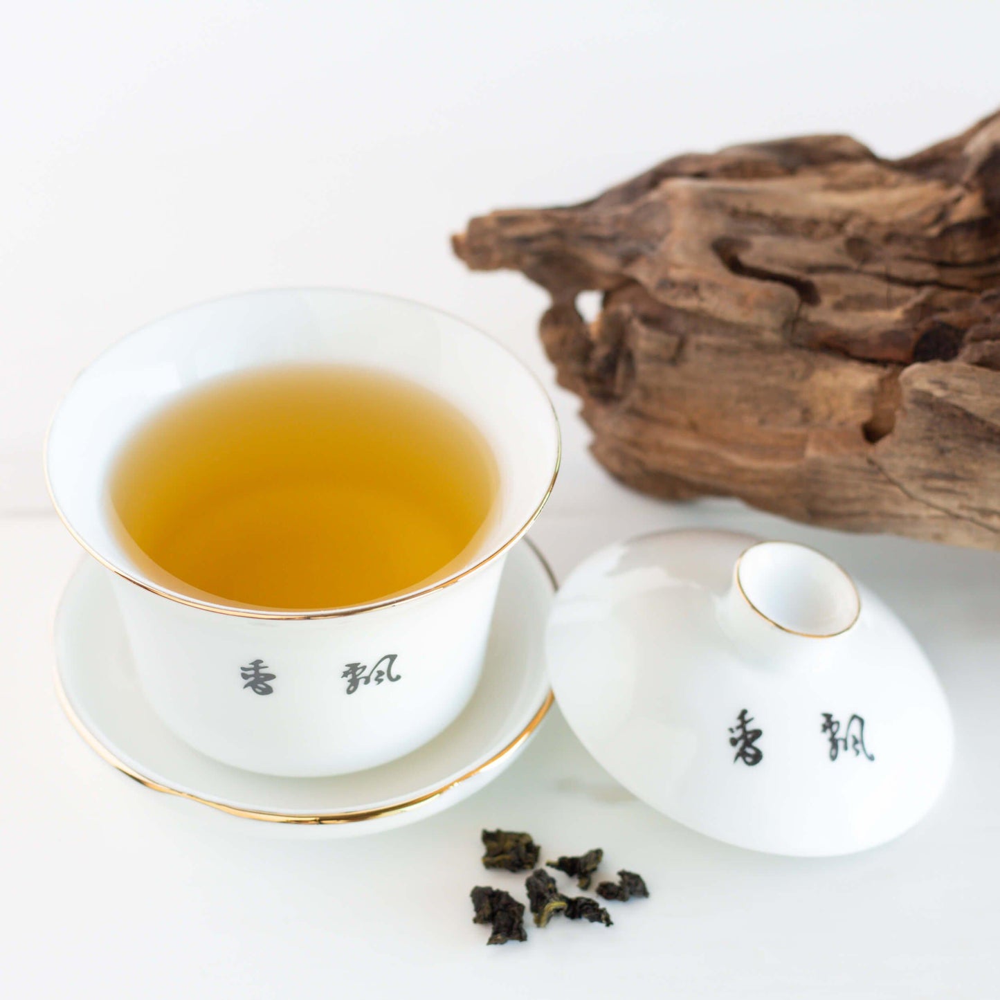 Milk Oolong Tea shown as brewed tea in a white gaiwan cup with the lid off. A piece of driftwood is in the background