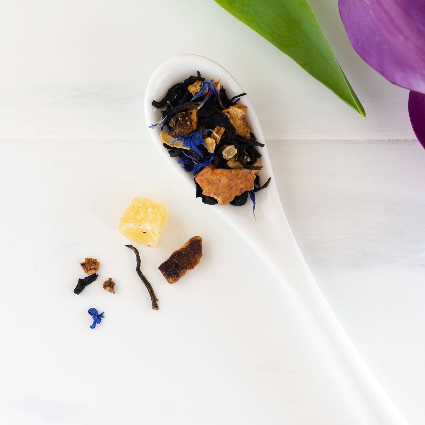 Lychee Purple Leaf Tea leaves and ingredients shown in a white ceramic spoon, with a few ingredients on the surface next to the spoon.