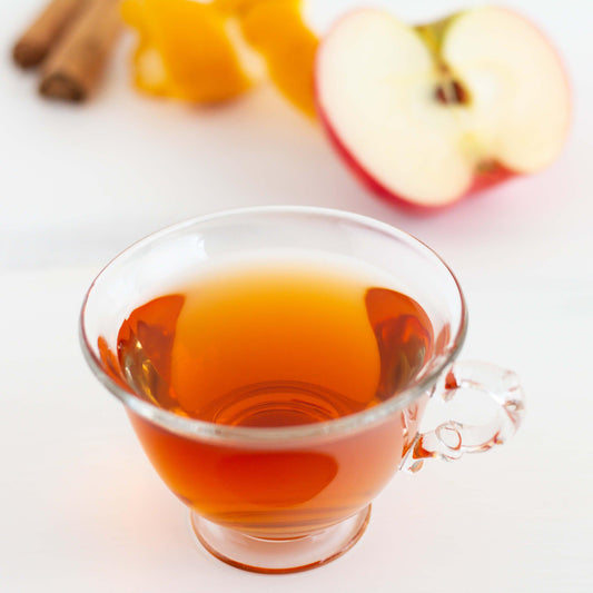 Honeybush Hot Cider Herbal Tea shown brewed in a clear mug surrounded by ingredients.