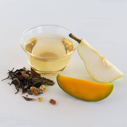 Mango Pear Organic White Tea shown brewed in a glass cup, surrounded by wedges of mango and pear as well as loose tea leaves