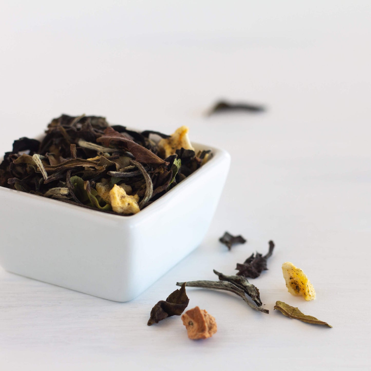 Mango Pear Organic White Tea shown in close up as loose tea leaves in a small square white dish with some tea leaves scattered nearby