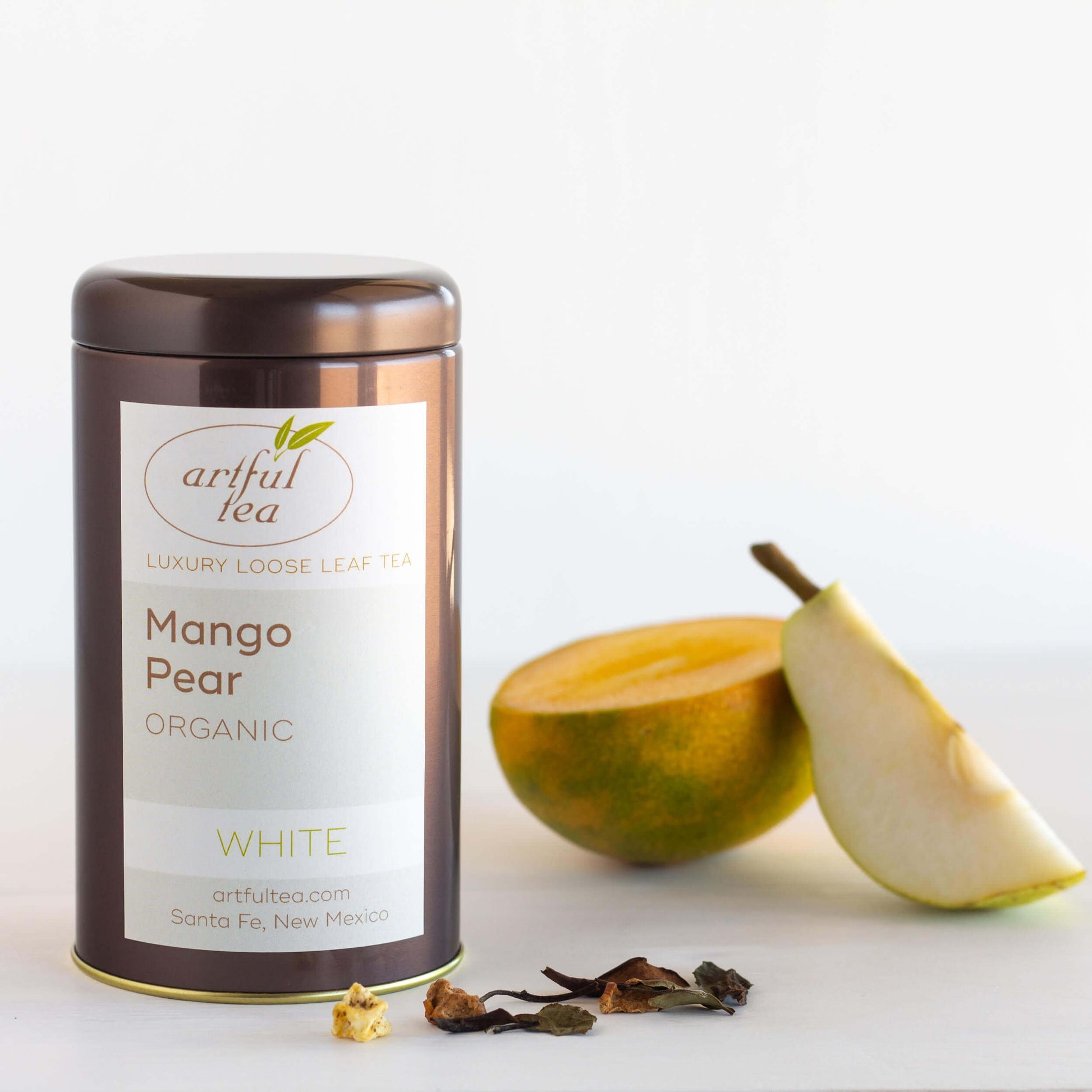 Mango Pear Organic White Tea shown packaged in a brown tin, with a sliced mango and a wedge of fresh pear nearby